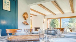 Un espace repas avec des nappes à rayures, des chaises en bois et une vue sur les arbres à travers de grandes fenêtres.