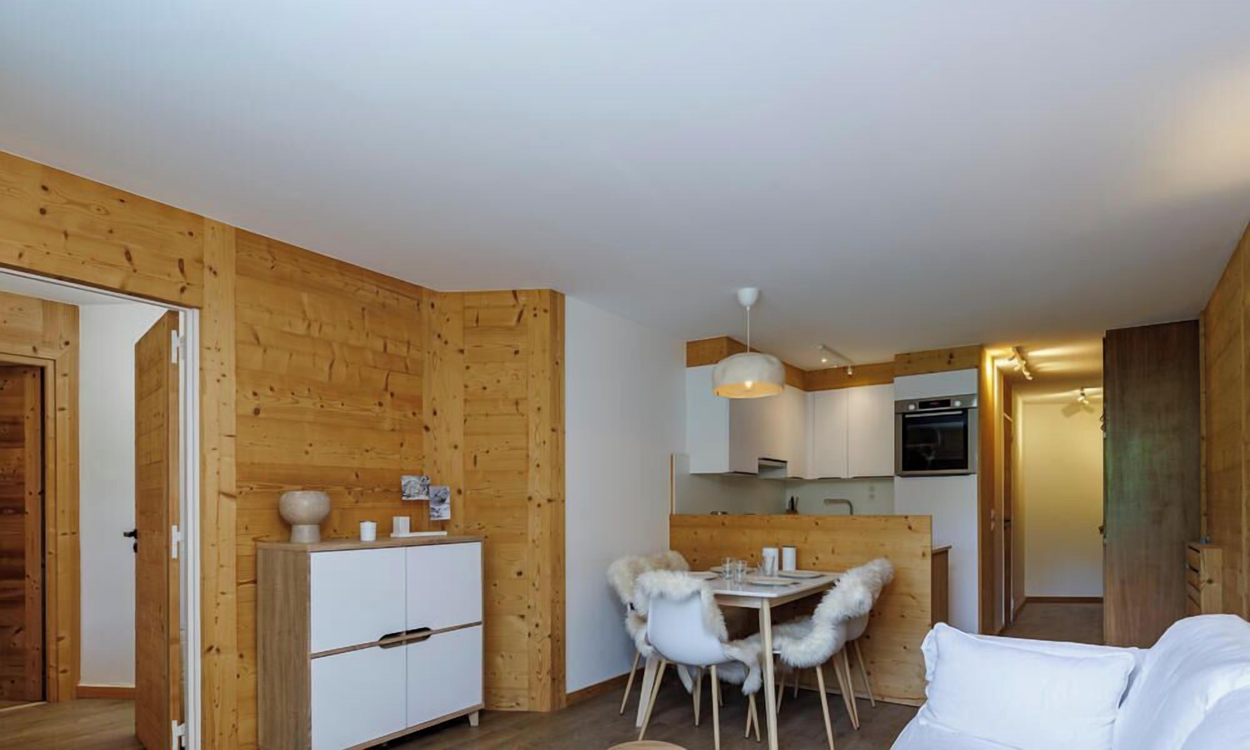 A wooden interior with a dining area, white furniture, and a kitchenette.