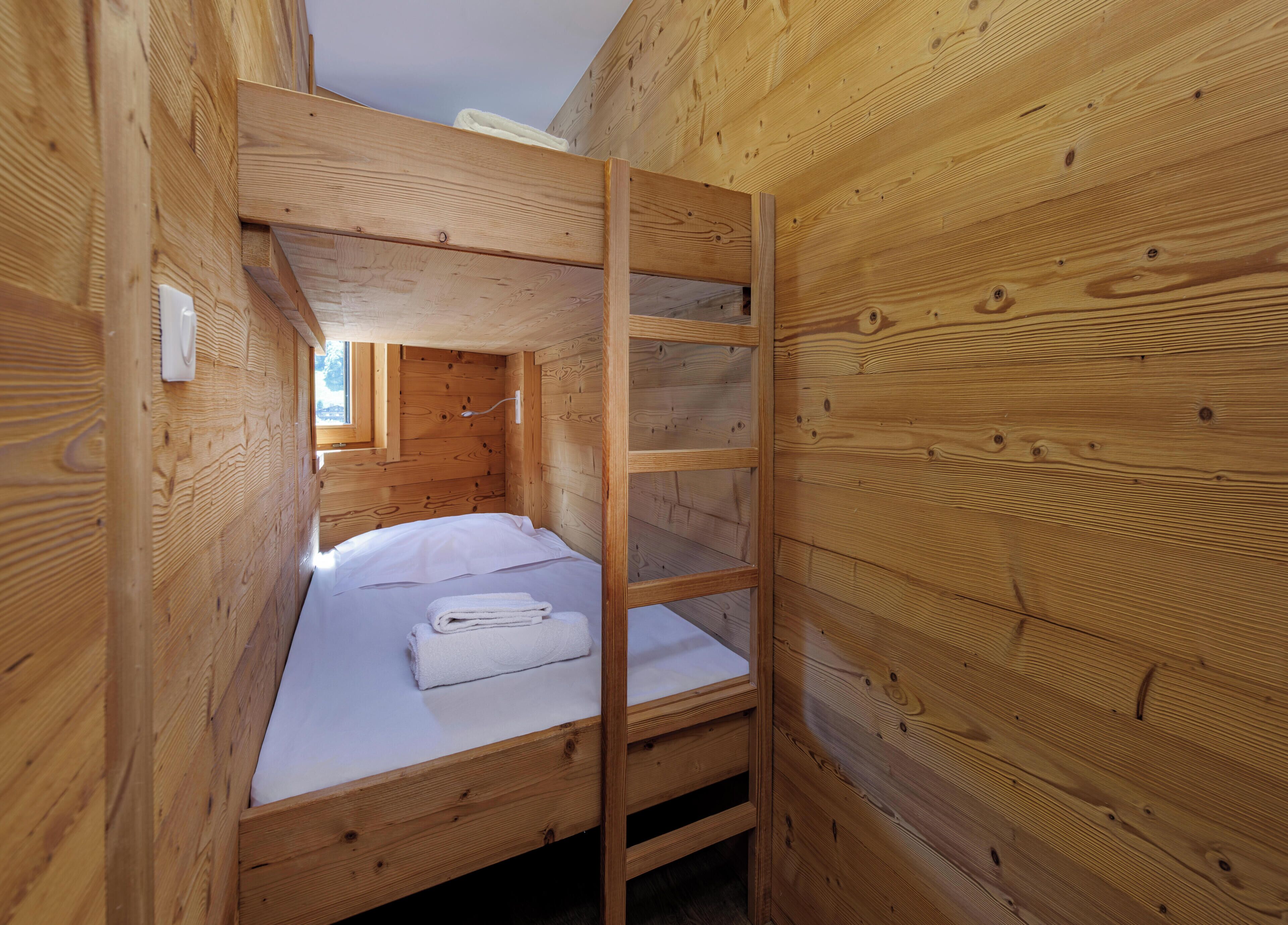A wooden cabin room with a bunk bed, a ladder, and a window.
