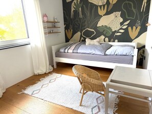 A bedroom with a bed, a desk, a chair, a window, and a wall with a nature-themed mural.