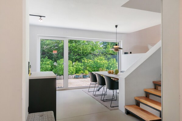 A modern interior with a dining area, a staircase, and a view of greenery outside.