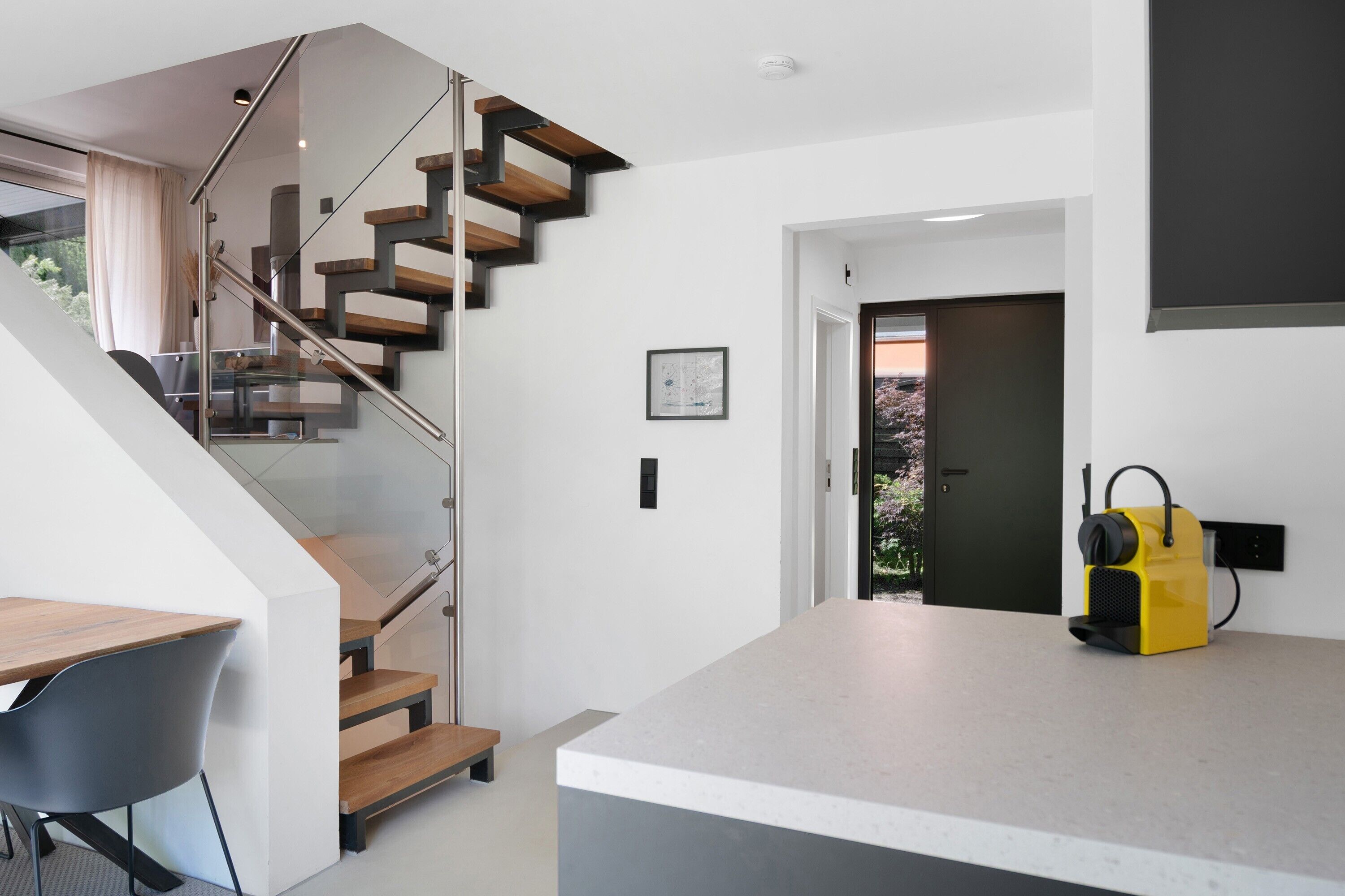 Ein modernes Interieur mit Treppe, Kücheninsel und einer Tür zum Außenbereich.