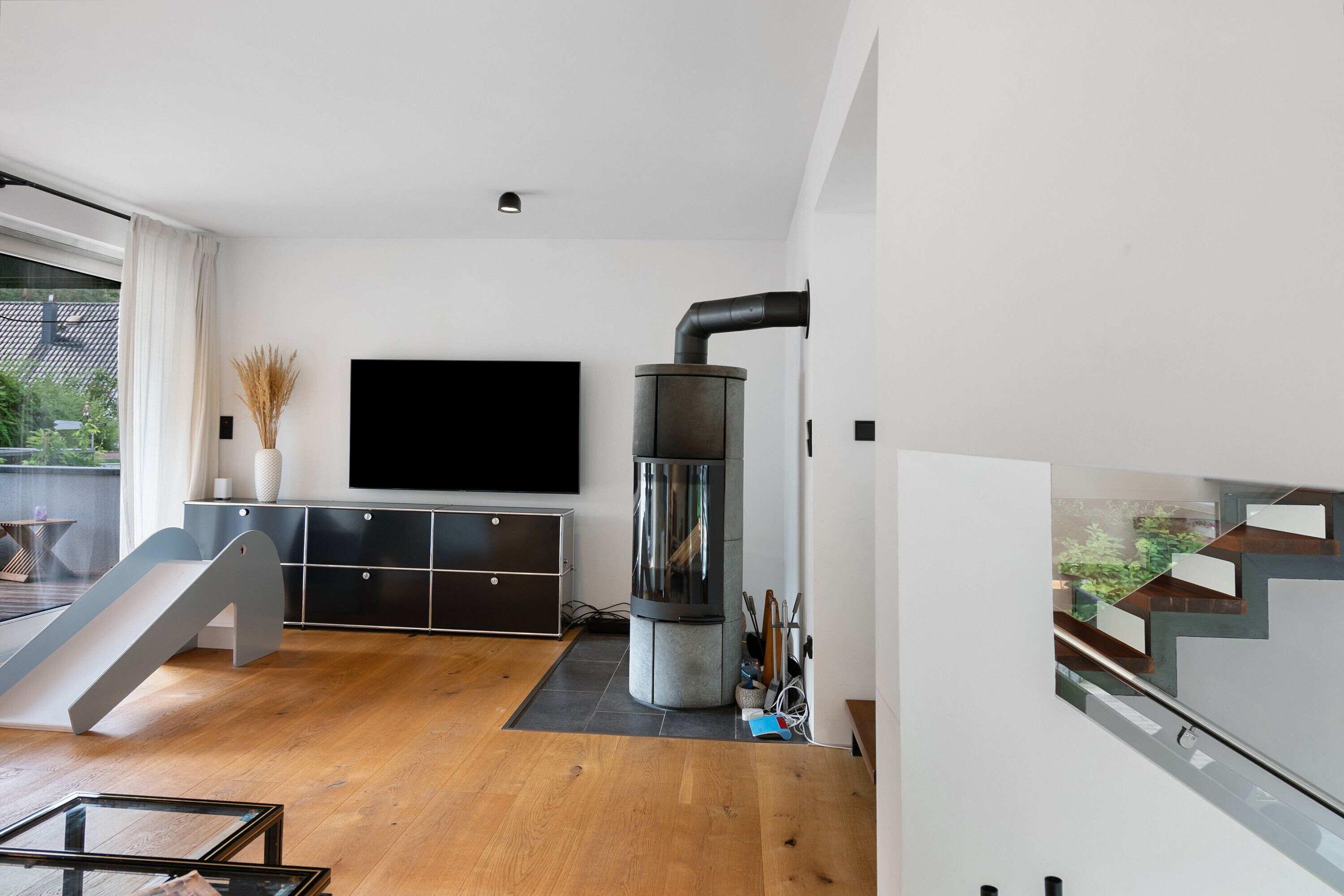 Una sala de estar moderna con un televisor de pantalla plana, una chimenea integrada, una escalera y una mesa de vidrio.
