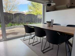 A modern dining area with a wooden table, black chairs, and a view of a garden through large windows.