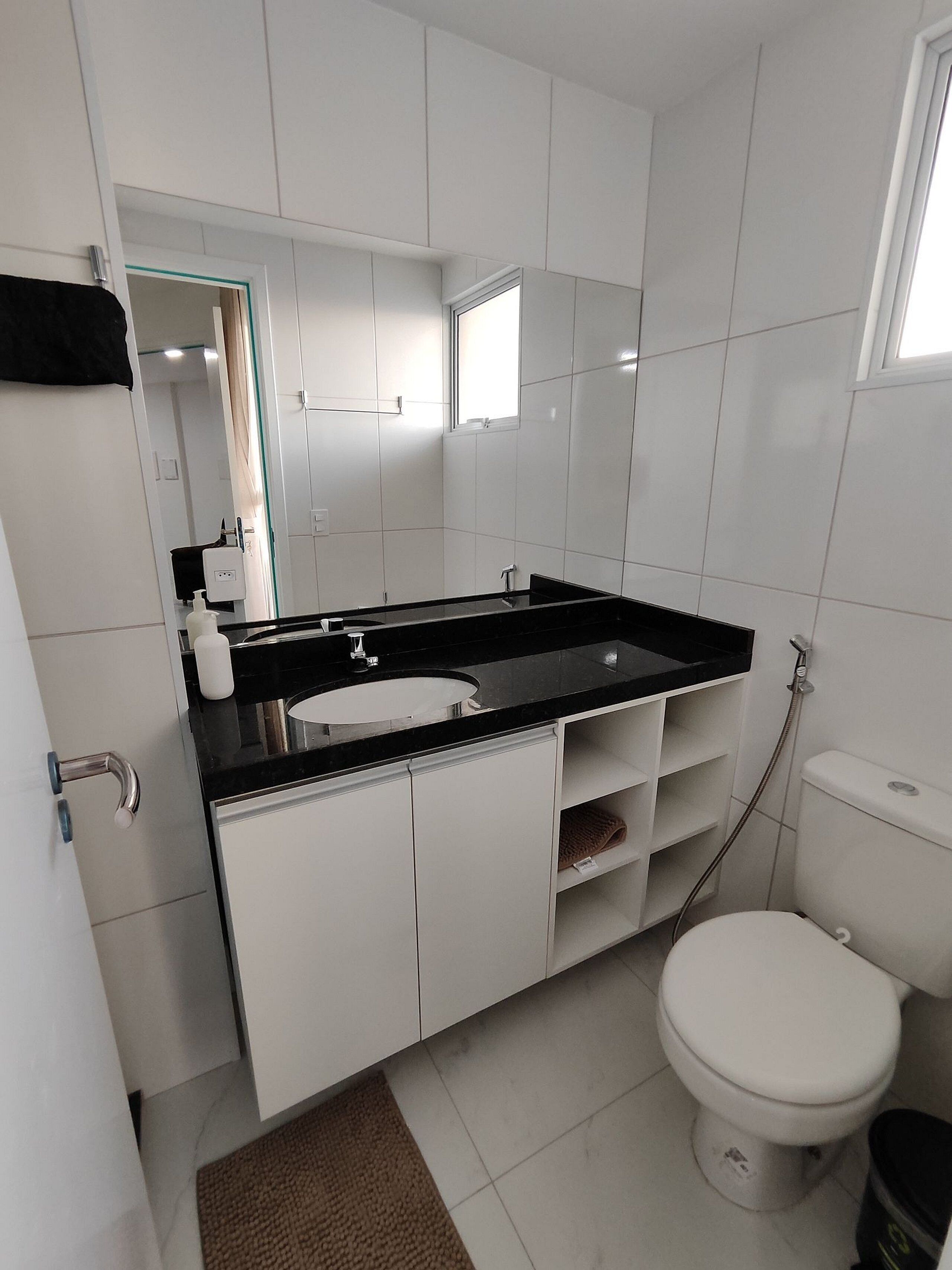 Une salle de bain moderne avec un lavabo noir sur un plan de toilette, des meubles blancs, des toilettes et une douche.