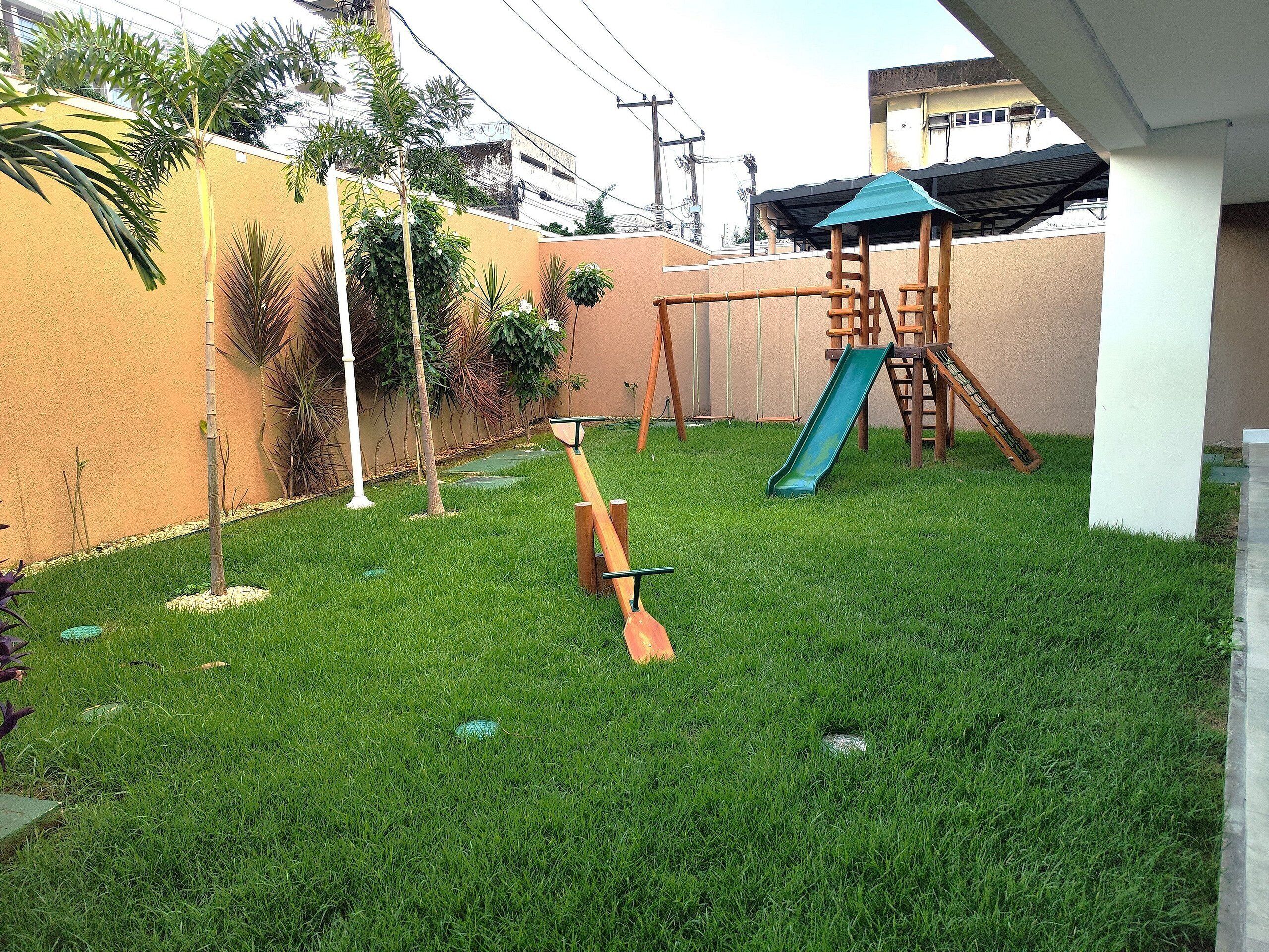 Un jardin avec un toboggan, une balançoire et un petit arbre.