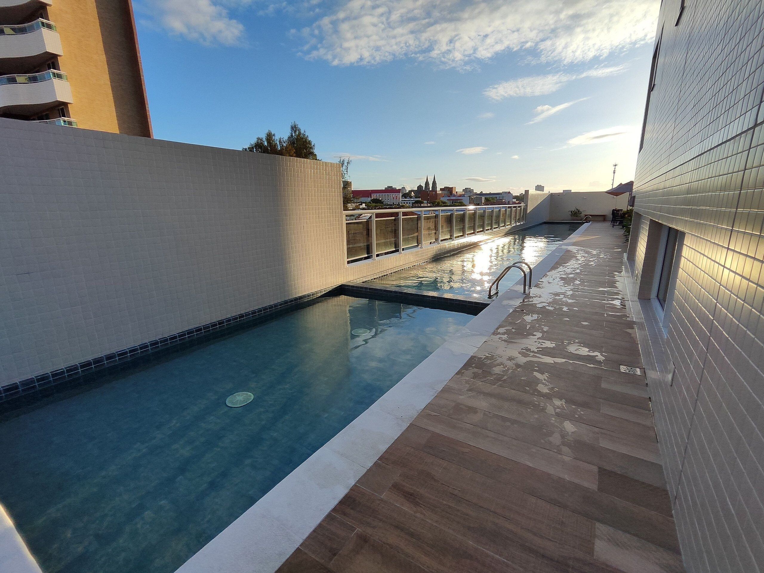 A rooftop pool with a clear view of the city skyline, a tiled deck, and a modern building facade.