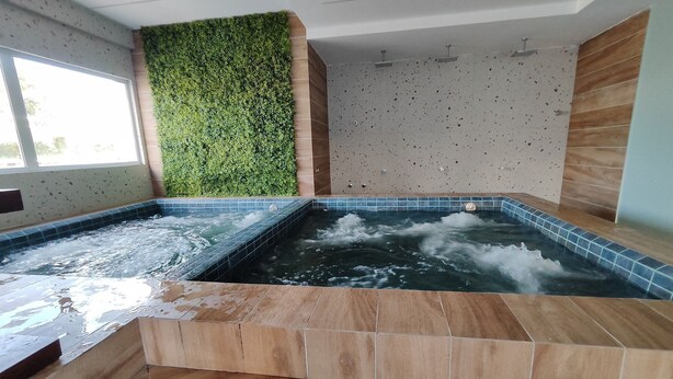 Ein Wellnessbereich mit zwei Whirlpools, einer grünen Wand und einem gefliesten Boden.