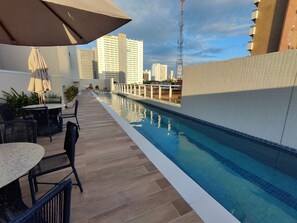 Ein Pool auf dem Dach mit Blick auf hohe Gebäude, Sitzgelegenheiten im Freien und einer Kachelwand.
