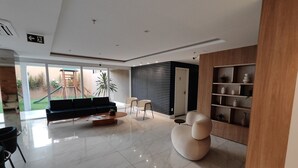 Ein modernes Wohnzimmer mit einer Couch, einem Couchtisch und Sesseln, einem Holzregal und Blick auf einen Spielplatz.