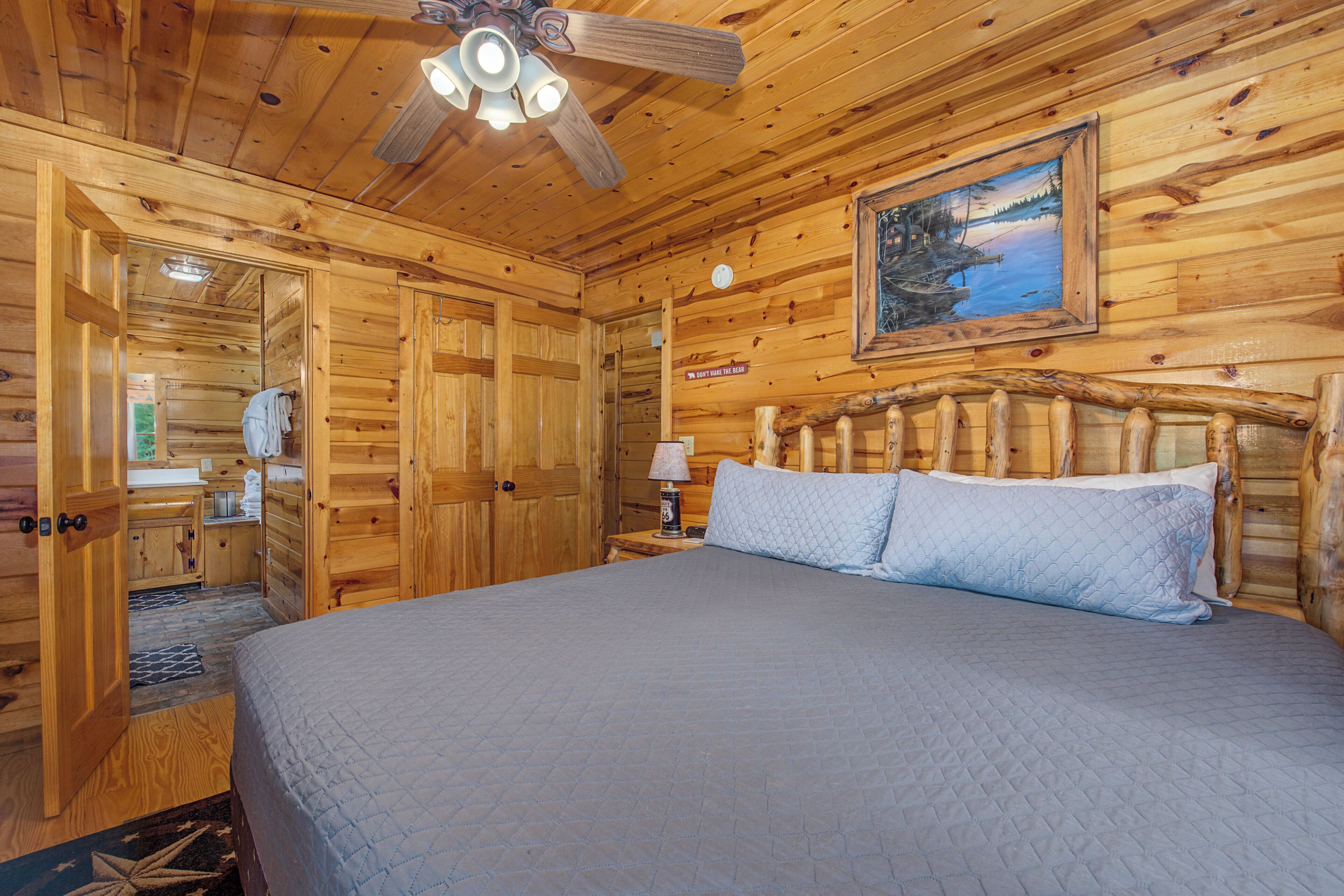 Ein Schlafzimmer in einer Holzhütte mit einem Bett, einem Deckenventilator, einem Gemälde und einem Holz-Kopfende.