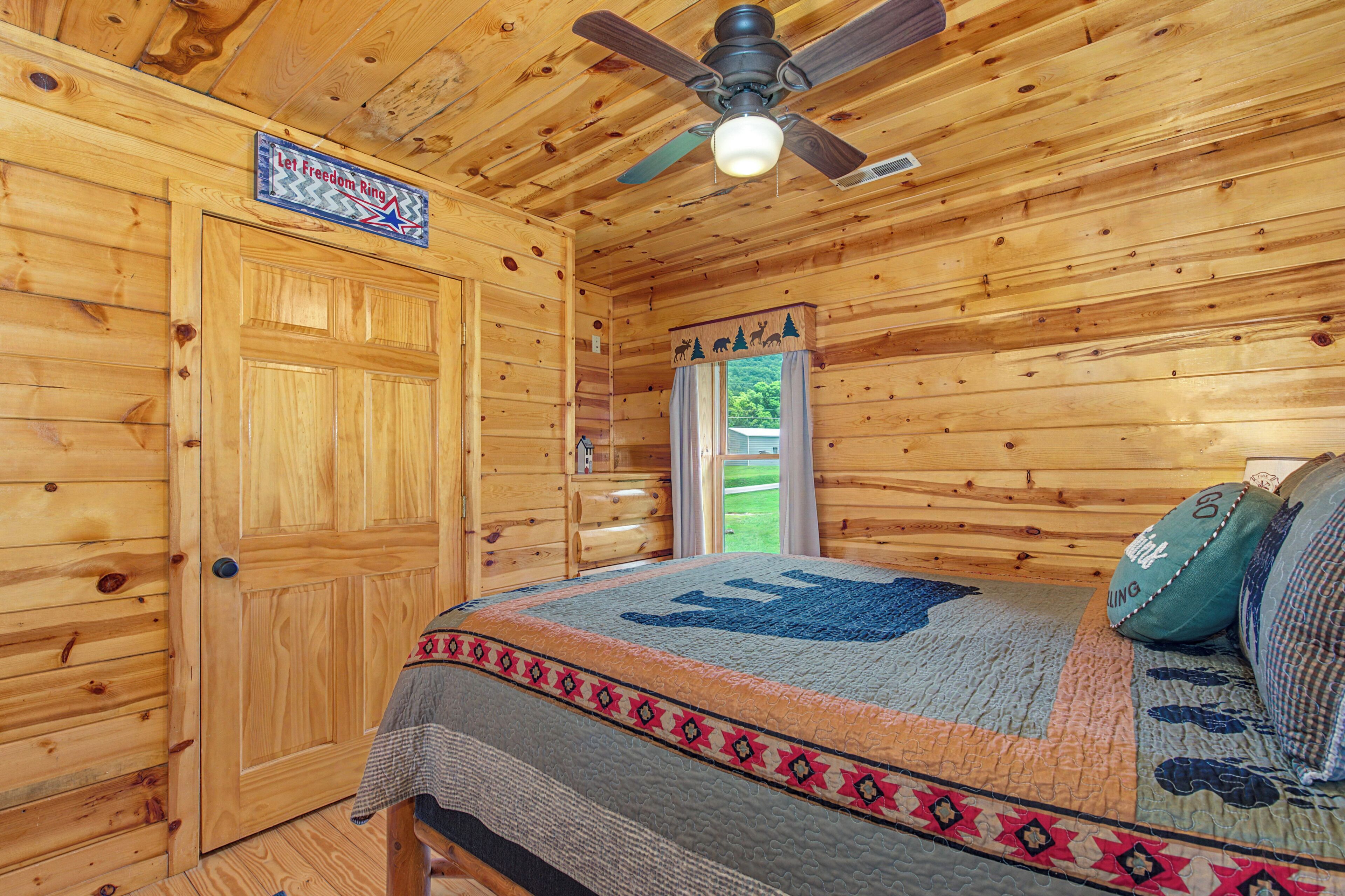 Une pièce de cabane en bois comprenant un lit, un ventilateur de plafond et une porte sur laquelle est affiché le message : « Que la liberté résonne ».