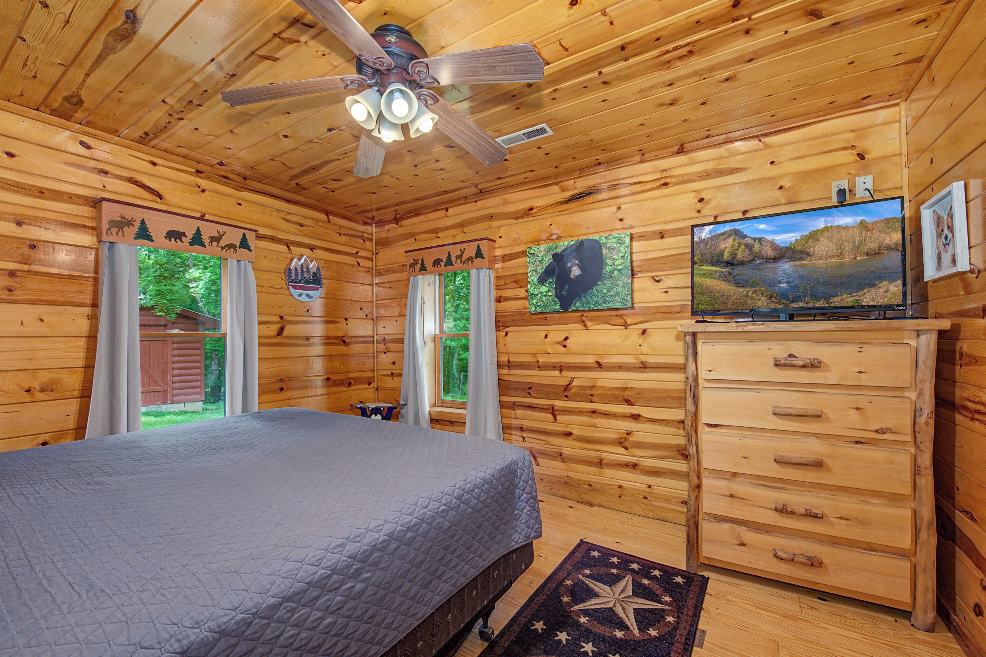 A log cabin room with a bed, a ceiling fan, a TV, and a dresser.