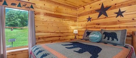 A log cabin bedroom with a bed, star decorations, a window with curtains, and a view of the outdoors.