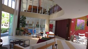A spacious lobby with a high ceiling, a seating area with a sofa and chairs, a staircase to an upper level, and a large window with a view of palm trees. - Bech Living (Aquiraz)