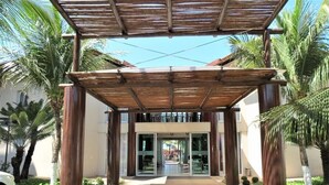 A covered entrance with a pathway leading to a building, surrounded by greenery and palm trees. - Bech Living (Aquiraz)