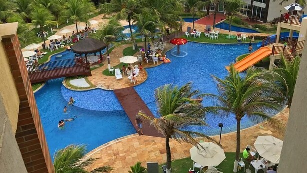 A hotel pool area with multiple swimming pools, palm trees, and outdoor seating. - Bech Living (Aquiraz)