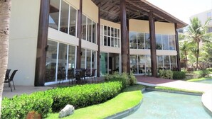 A modern hotel with a pool, large windows, and a covered outdoor area. - Bech Living (Aquiraz)