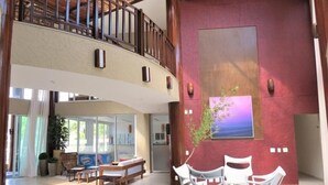 A spacious lobby with a high ceiling, a balcony, a large window, and a seating area with white chairs. - Bech Living (Aquiraz)