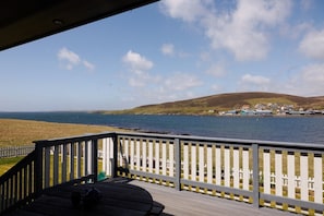 A wooden deck with a railing overlooking a beach and a coastal town. - Modern Coastal Stay, Stunning Views, Private Garden (Trondra)