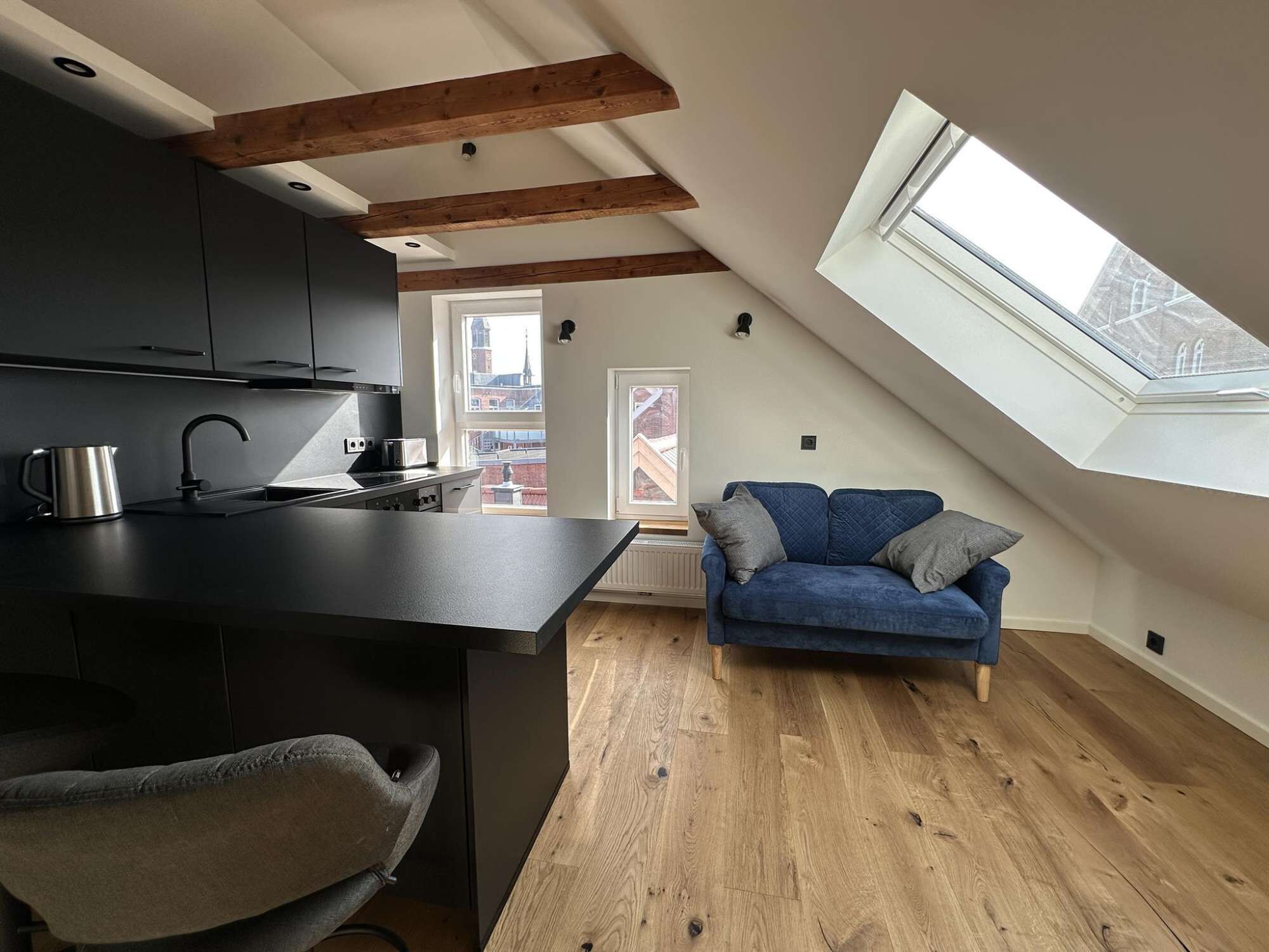 Een modern loft appartement met keuken, eethoek, een blauwe bank en een dakraam.