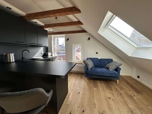 A modern loft apartment with a kitchen, a dining area, a blue sofa, and a skylight.