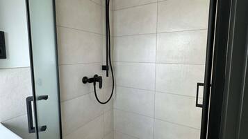 Une douche avec une porte en verre, des murs recouverts de carreaux blancs et un plafond avec une poutre en bois.