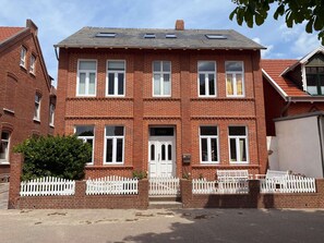 Ein zweistöckiges Backsteinhaus mit weißem Zaun, einer Garagentür und einer sichtbaren Hausnummer.
