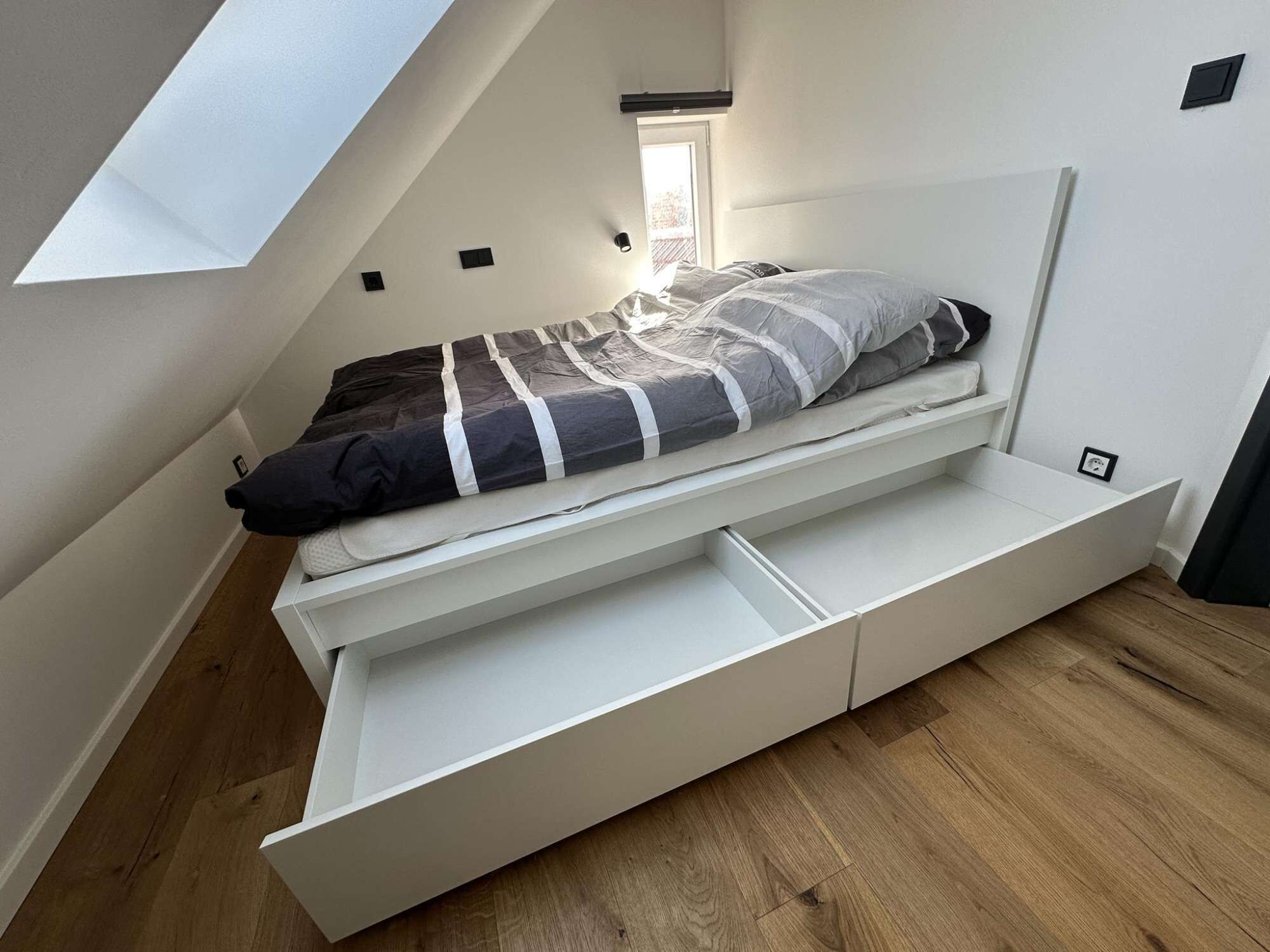 Ein Schlafzimmer im Loft-Stil mit Bett, eingebauten Schubladen, einem Oberlicht und einem Fenster.