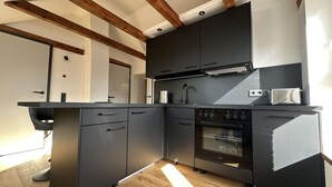 A modern kitchen with dark cabinetry, a built-in oven, and a wooden ceiling. - Stylish BERNHARD Apartment in STRAND HAUS 10 (Borkum)