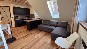 Ein Loft-Zimmer mit Küche, einer Couch, einem Esstisch und einem kleinen Fenster.