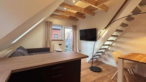 Ein Schlafzimmer im Loft-Stil mit einem Holztisch, einer Couch, einem Sessel, einem Fernseher und einer Treppe.