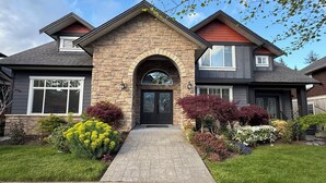 A two-story house with a stone facade, a central entrance with an arch, and a brick pathway leading to the door.