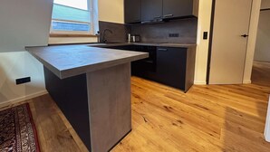 A modern kitchen with a central island, dark cabinetry, and a window providing natural light. - Stylish OSTEREMS Apartment in STRAND HAUS 10 (Borkum)
