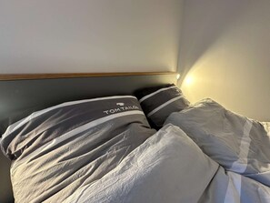 A bed with gray bedding and pillows, a wooden headboard, and a light source casting a shadow on the wall. - Stylish OSTEREMS Apartment in STRAND HAUS 10 (Borkum)