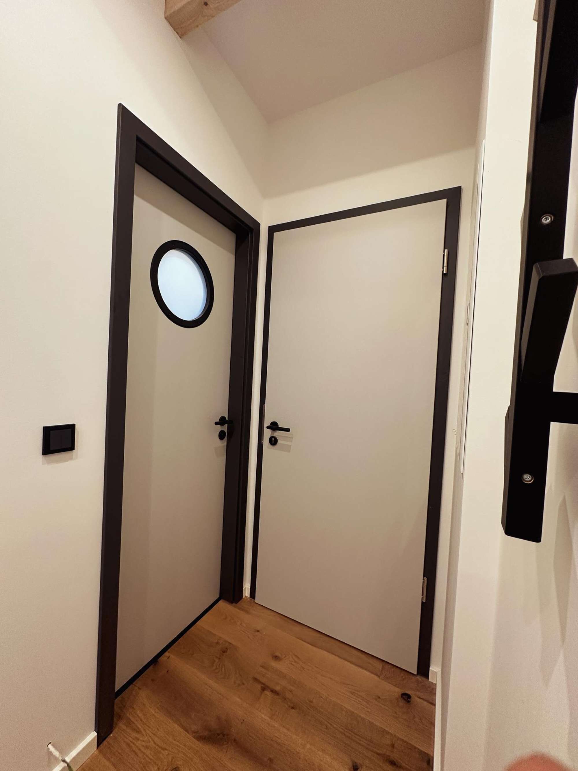 Ein Flur mit zwei Türen, davon eine mit rundem Fenster, und Holzdielen.