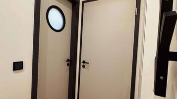 Ein Flur mit zwei Türen, davon eine mit rundem Fenster, und Holzdielen.