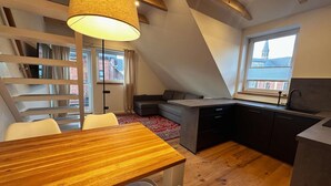 A modern loft apartment with a dining area, kitchen, and a large window offering a city view. - Stylish OSTEREMS Apartment in STRAND HAUS 10 (Borkum)