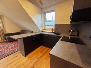 A compact kitchen with a built-in stove, a sink, and a window overlooking a cityscape. - Stylish OSTEREMS Apartment in STRAND HAUS 10 (Borkum)
