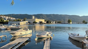 Ein ruhiger Hafen mit vertäuten Booten, einer Anlegestelle und im Hintergrund Gebäuden und Hügeln.