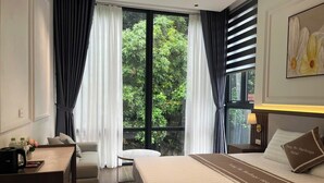 Una habitación de hotel con cama, escritorio, silla y ventana con cortinas.
