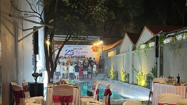 Un espacio para eventos al aire libre con mesas y sillas, un escenario con un cartel y una zona de piscina.