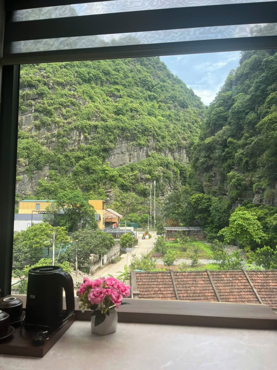 Blick aus einem Fenster auf ein üppiges Tal mit einem Gebäude und einem Kaffeeautomaten auf dem Fensterbrett.