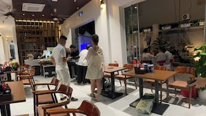 Un restaurante con mesas y sillas de madera, una barra con personal y una pared decorativa.