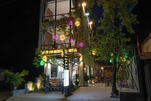 Entrada de un hotel con un letrero de neón, asientos al aire libre y luces decorativas.