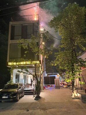 Um hotel com letreiro de neon, um pátio pavimentado e um carro estacionado.