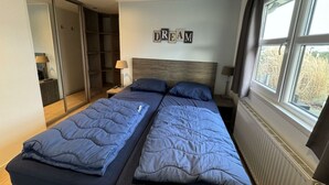 A bedroom with two beds, a wardrobe, a window with curtains, and a wall-mounted sign that reads 'DREAM'. - Holiday Home in Noordwijk With Terrace (Noordwijk)