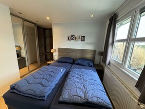 A bedroom with two beds, a wardrobe, a window with curtains, and a wall-mounted sign that reads 'DREAM'. - Holiday Home in Noordwijk With Terrace (Noordwijk)