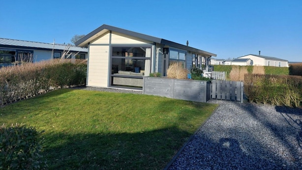 A modern house with a large glass window, a concrete pathway, and a grassy lawn. - Holiday Home in Noordwijk With Terrace (Noordwijk)