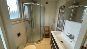 A modern bathroom with a glass shower enclosure, a white toilet, a wooden shelf, and a white sink with a mirror above it. - Holiday Home in Noordwijk With Terrace (Noordwijk)